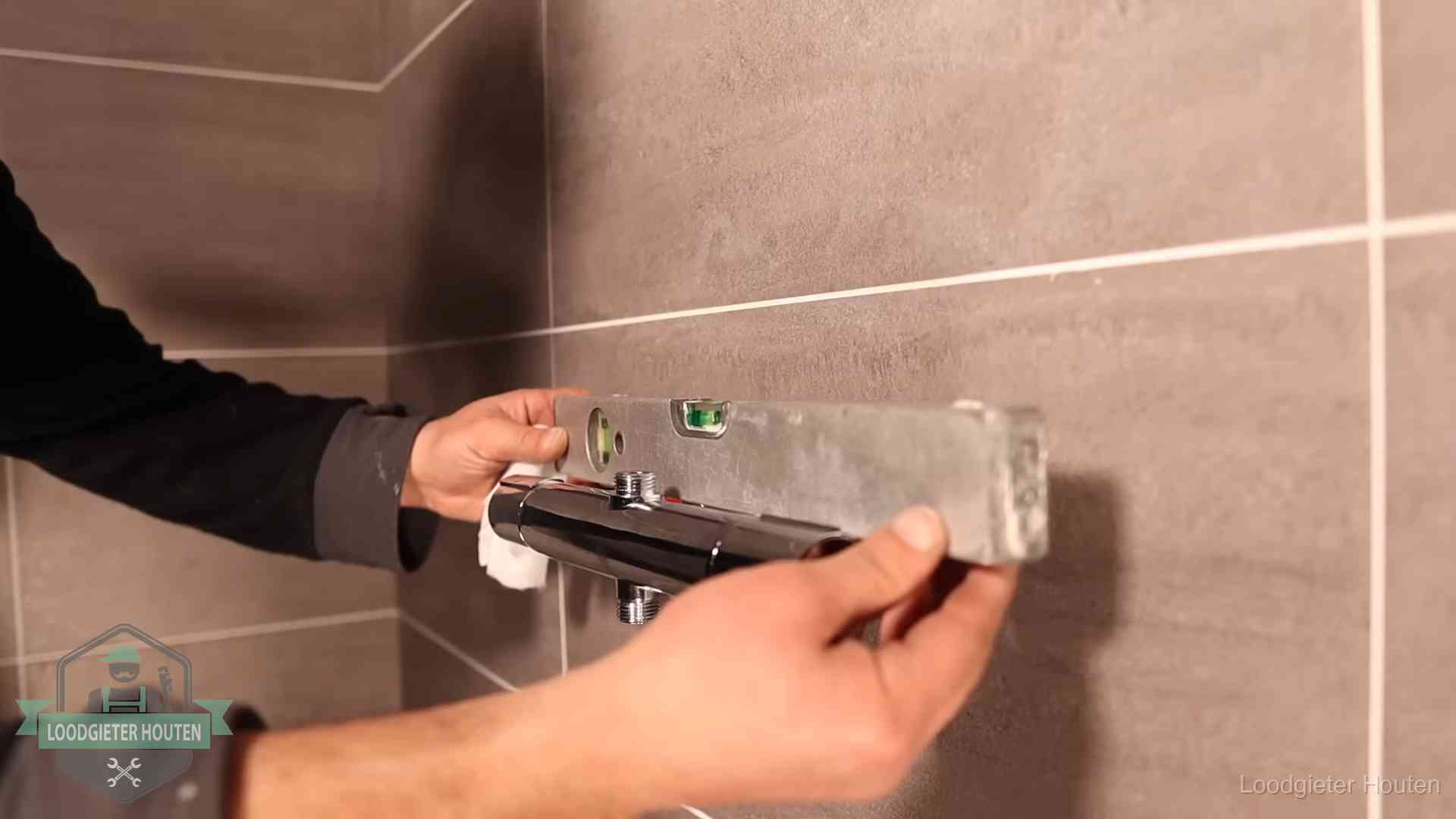 Loodgieter lijnt een douchekraan uit met een waterpas in een woning in Houten