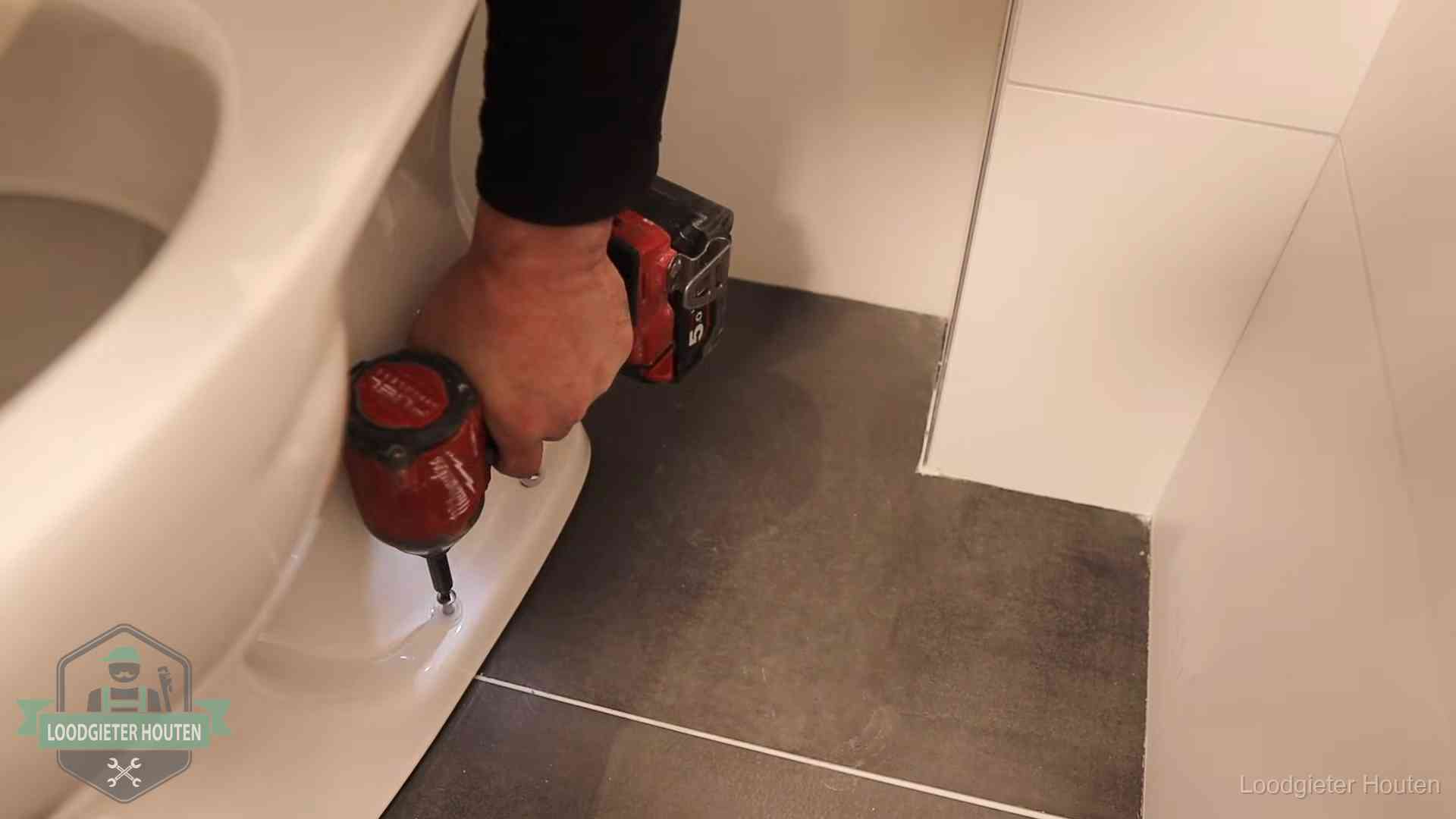 Kosten wc ontstoppen in Houten Loodgieter zet de voet van een wc-pot vast op de tegelvloer in Houten